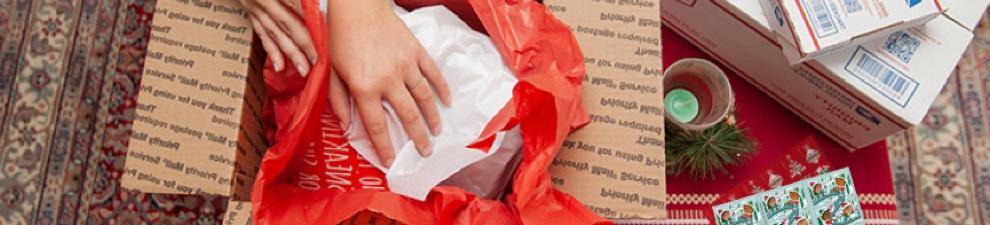 Young woman preparing holiday gifts and Priority Mail boxes to ship for December 25 delivery.